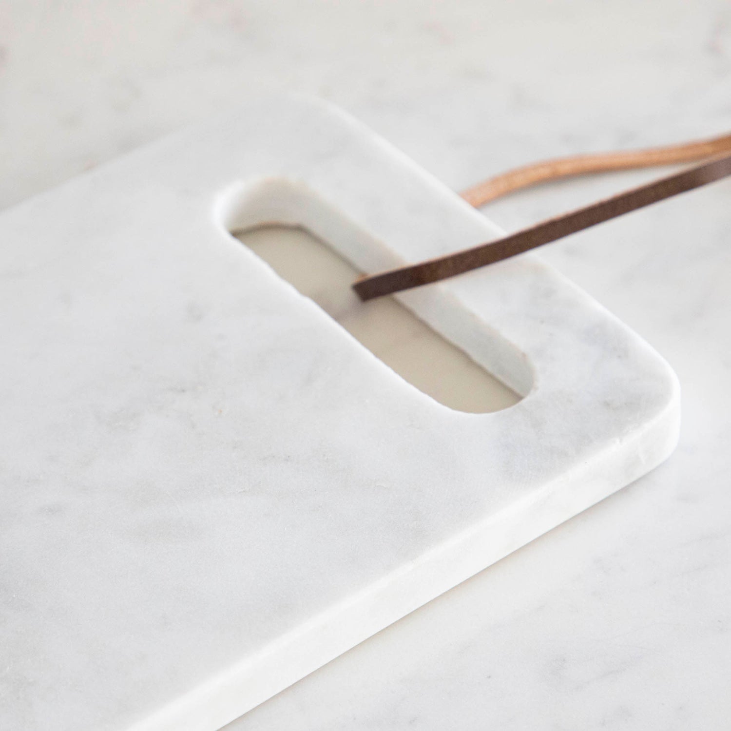 A White Marble Cheese Board  with a cutout made for holding and a brown loop for decoration.