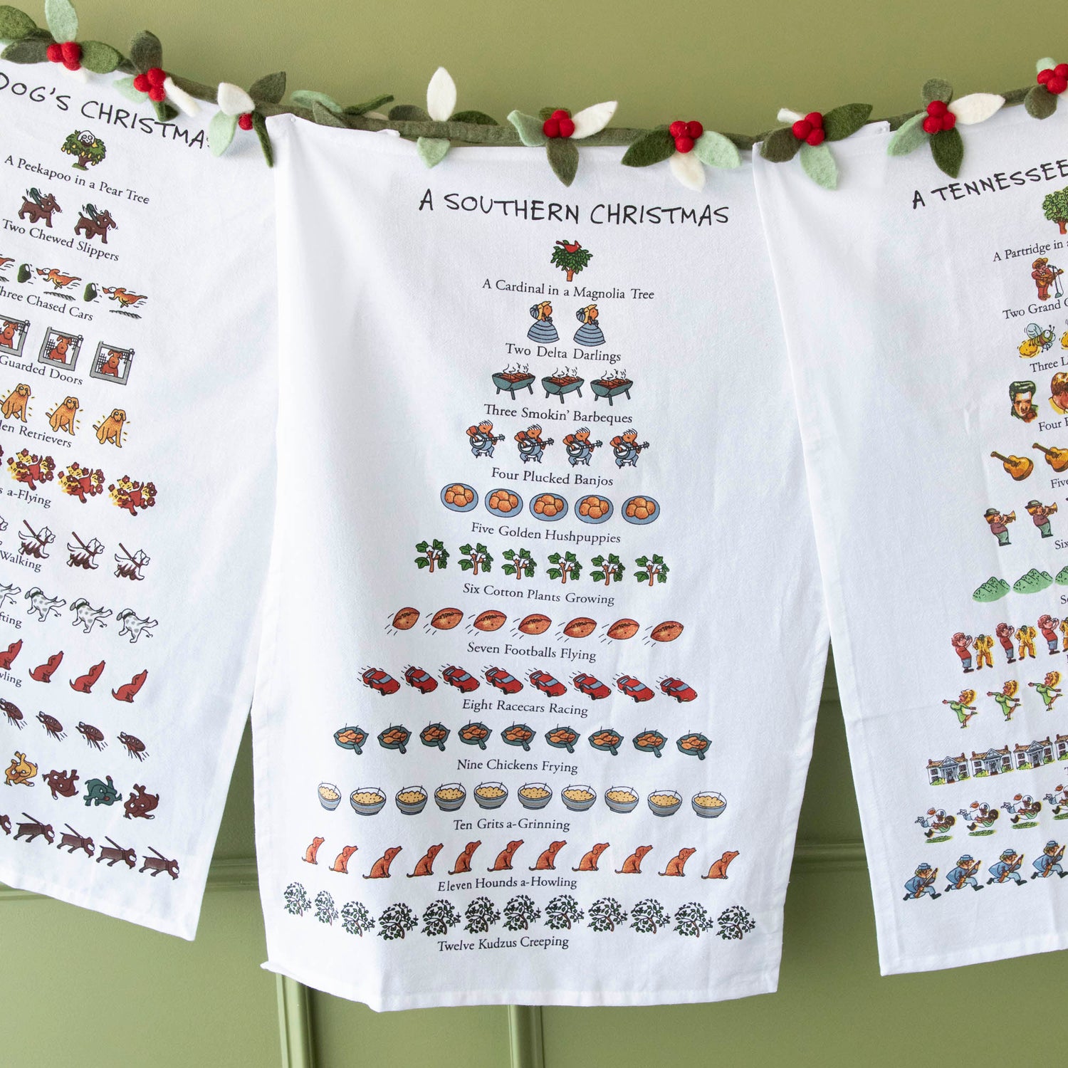 A Southern Christmas Print Kitchen Towel hung next to Christmas towels on a felt berry garland.