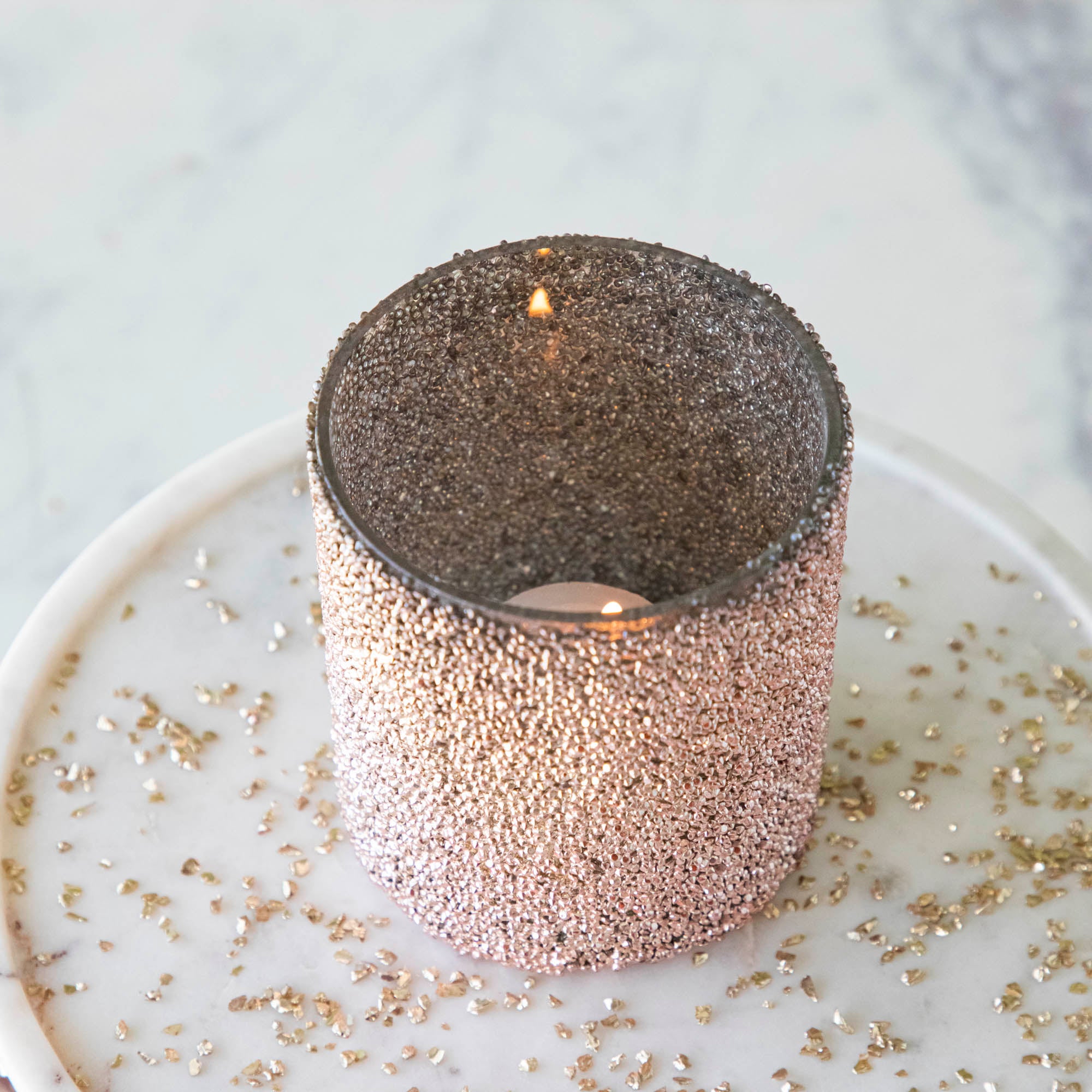 Pink Shimmer Votive surrounded by glitter with a lit tea light candle in the middle.