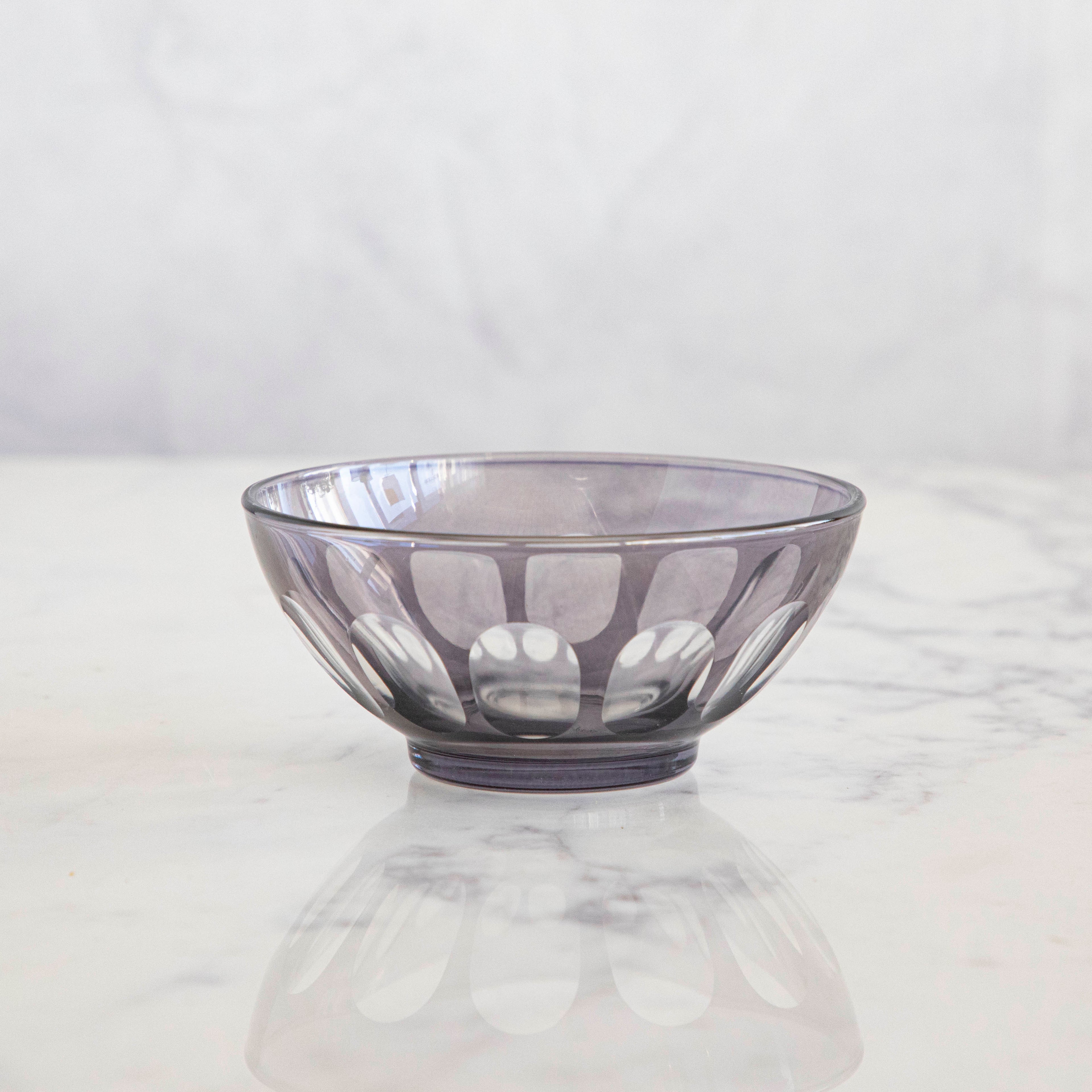 A Rialto Smoke Glass Bowl by SIR/MADAM on a marble surface with reflections below, reminiscent of Venice-inspired glassware.