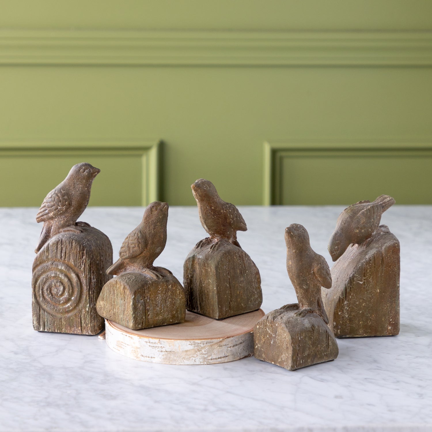 Set of wooden bird sculptures on a white surface with a green wall background.