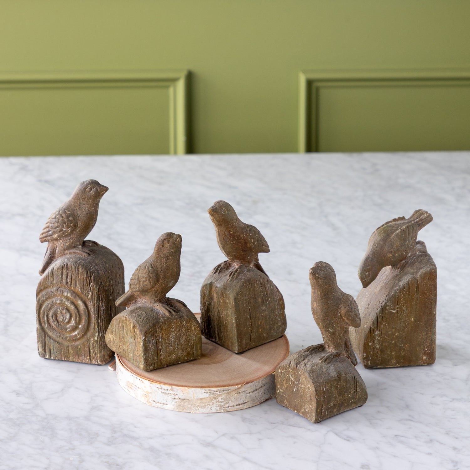 Set of wooden bird sculptures on a white surface with a green wall background.