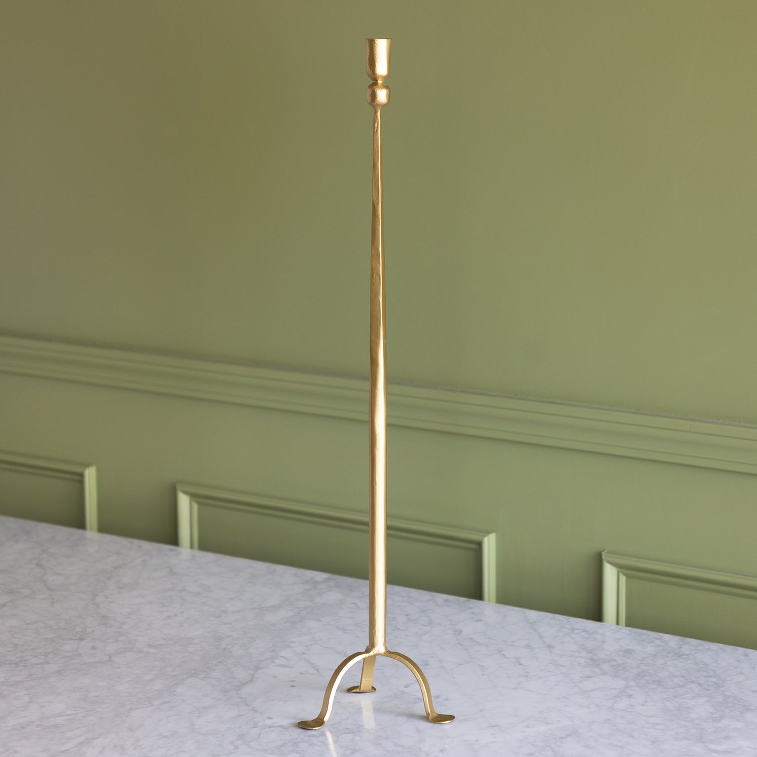 Gold candlestick on a marble surface with a green wall background