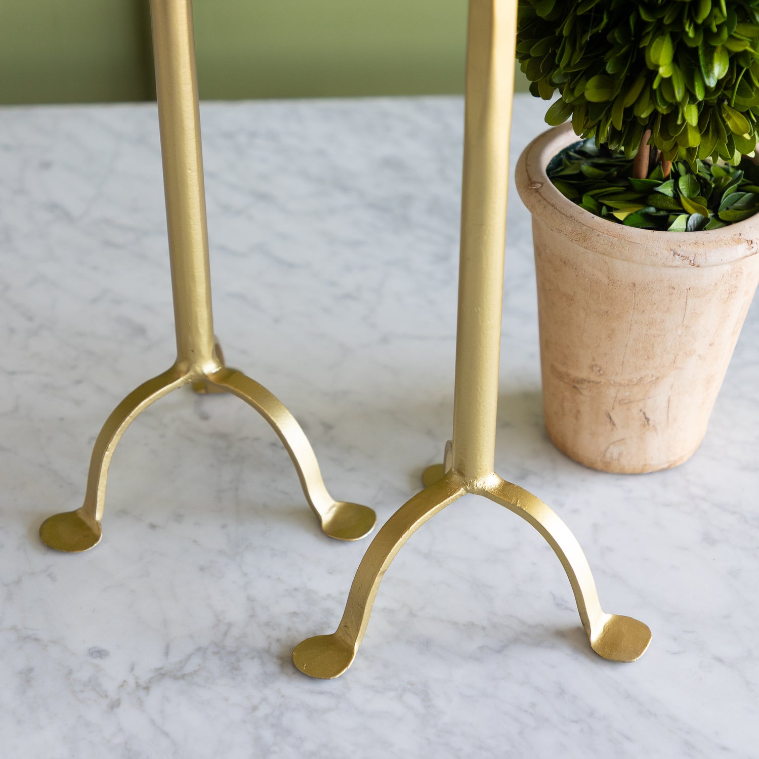 Gold candle holders on a marble surface with a potted plant in the background