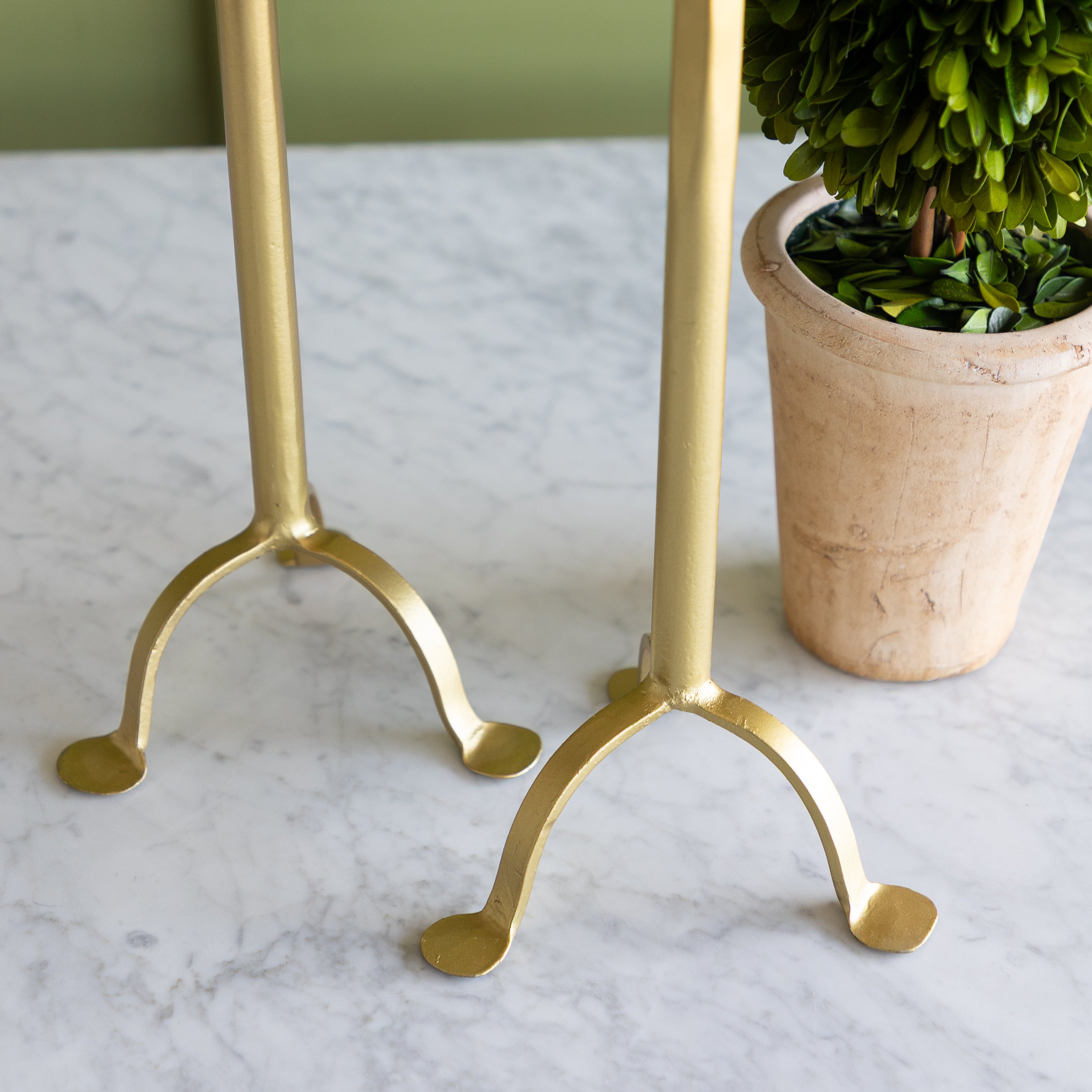 Gold candle holders on a marble surface with a potted plant in the background