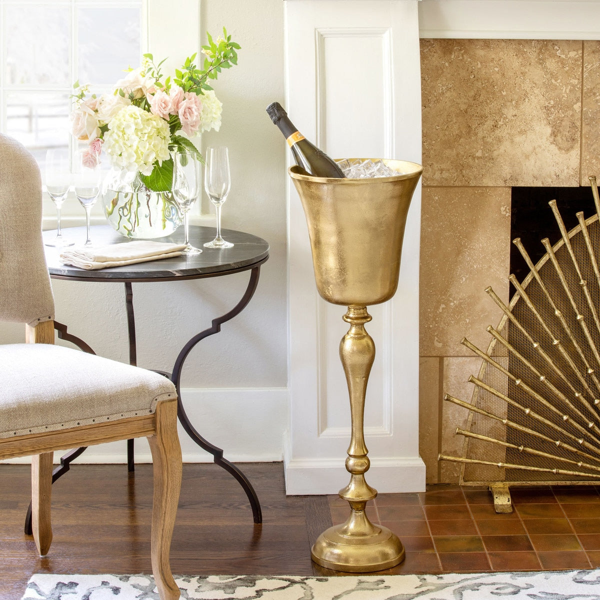 Gold wine cooler with champagne bottle in a stylish room with a fireplace and table.