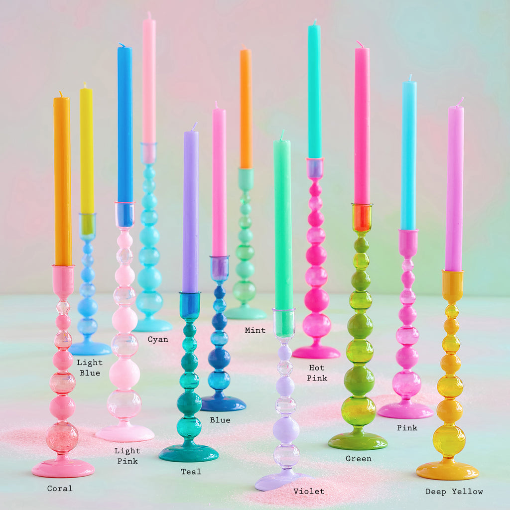 Colorful candles in various shades arranged in a gradient on a pastel background, displayed on Glitterville&