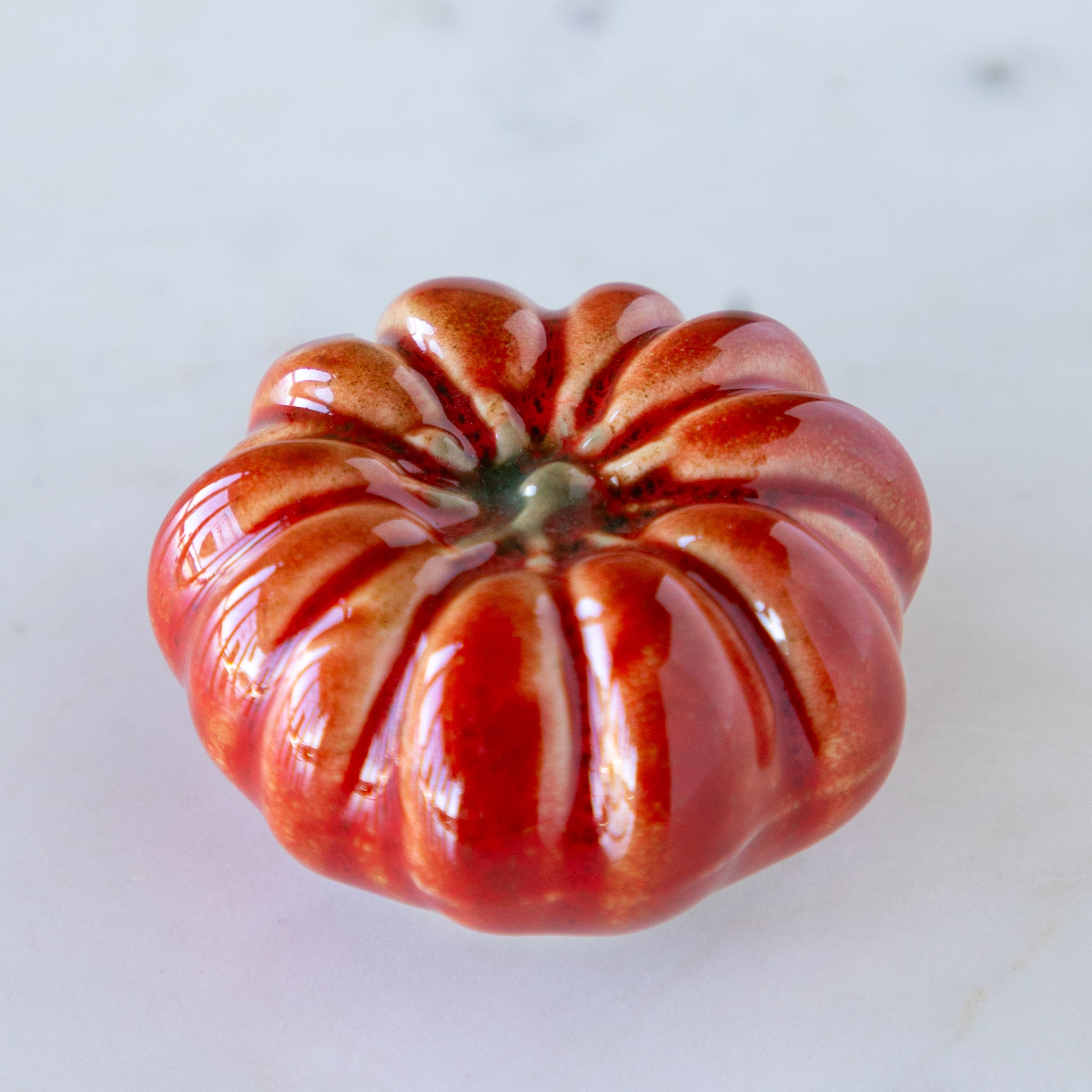 Ceramic tomato with a glossy finish on a light gray background.