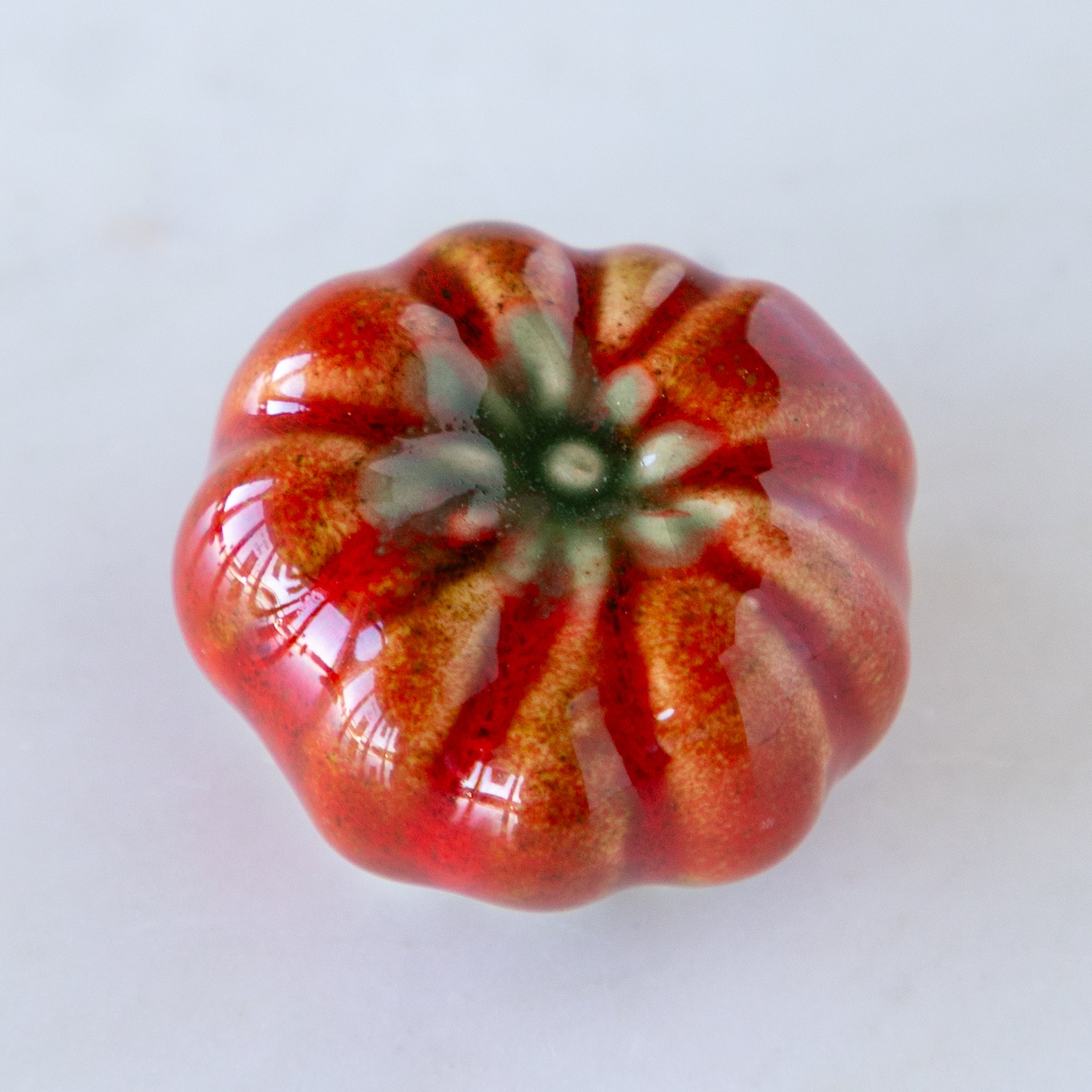 Decorative red and orange ceramic tomato on a white background.
