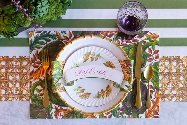 Decorative table setting with a name card, plates, and cutlery on a patterned placemat.
