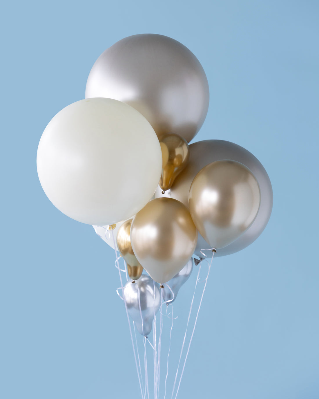 Bunch of balloons in white, gold, and silver on a light blue background.