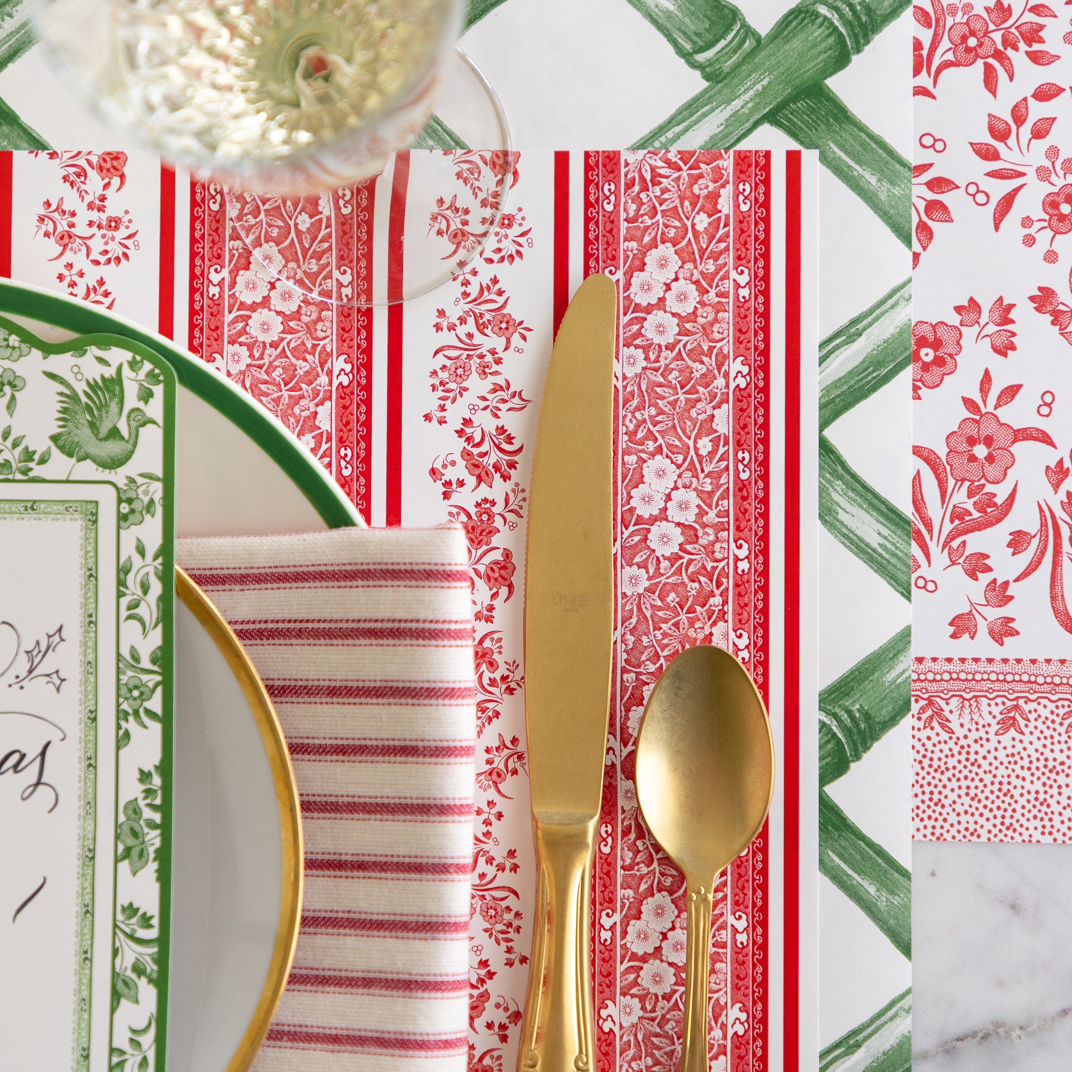 The Red Burleigh Stripe Placemat under an elegant place setting featuring gold flatware, a red stripe napkin and Green Lattice and Red Burleigh Runner underneath.