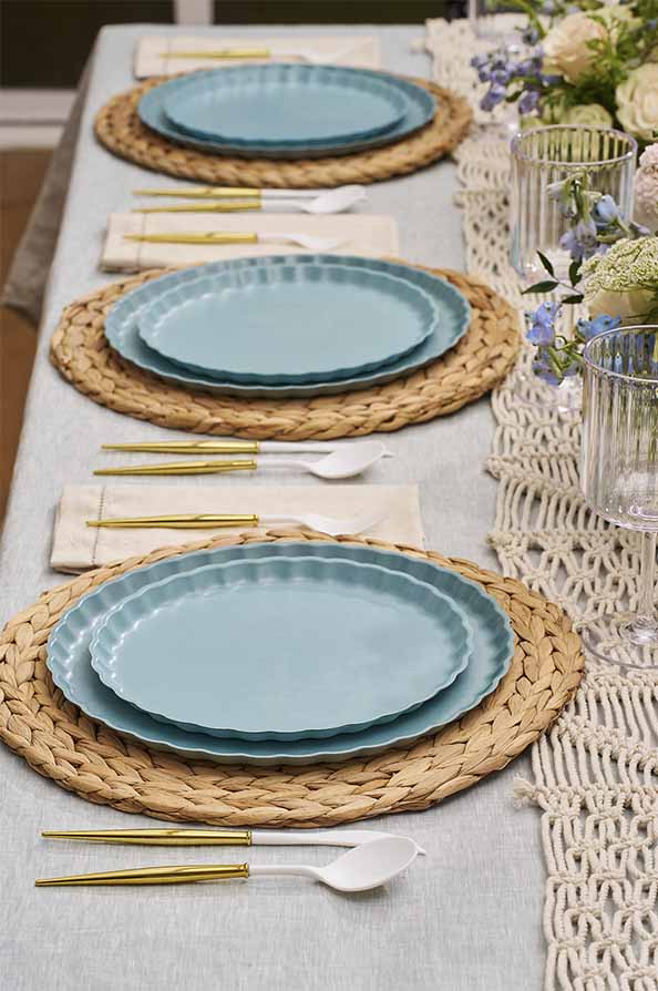 Table setting with blue plates, gold cutlery, and woven placemats on a light gray tablecloth.