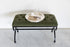 Green upholstered bench with a round metal tray on a white background