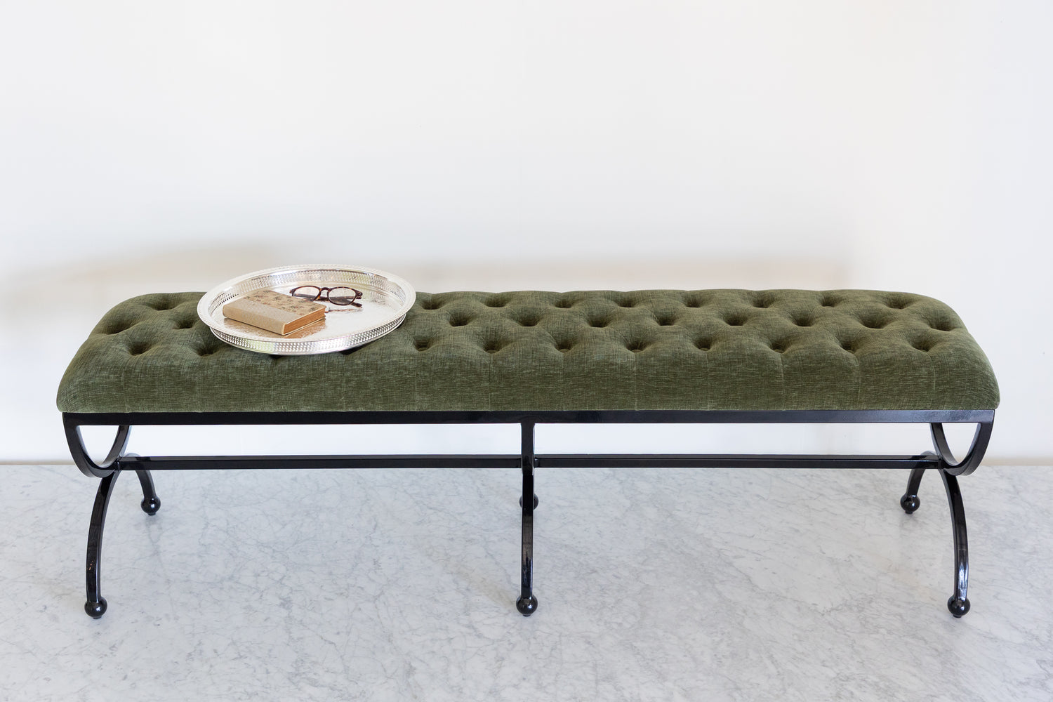 Green tufted bench with black metal legs on a white background