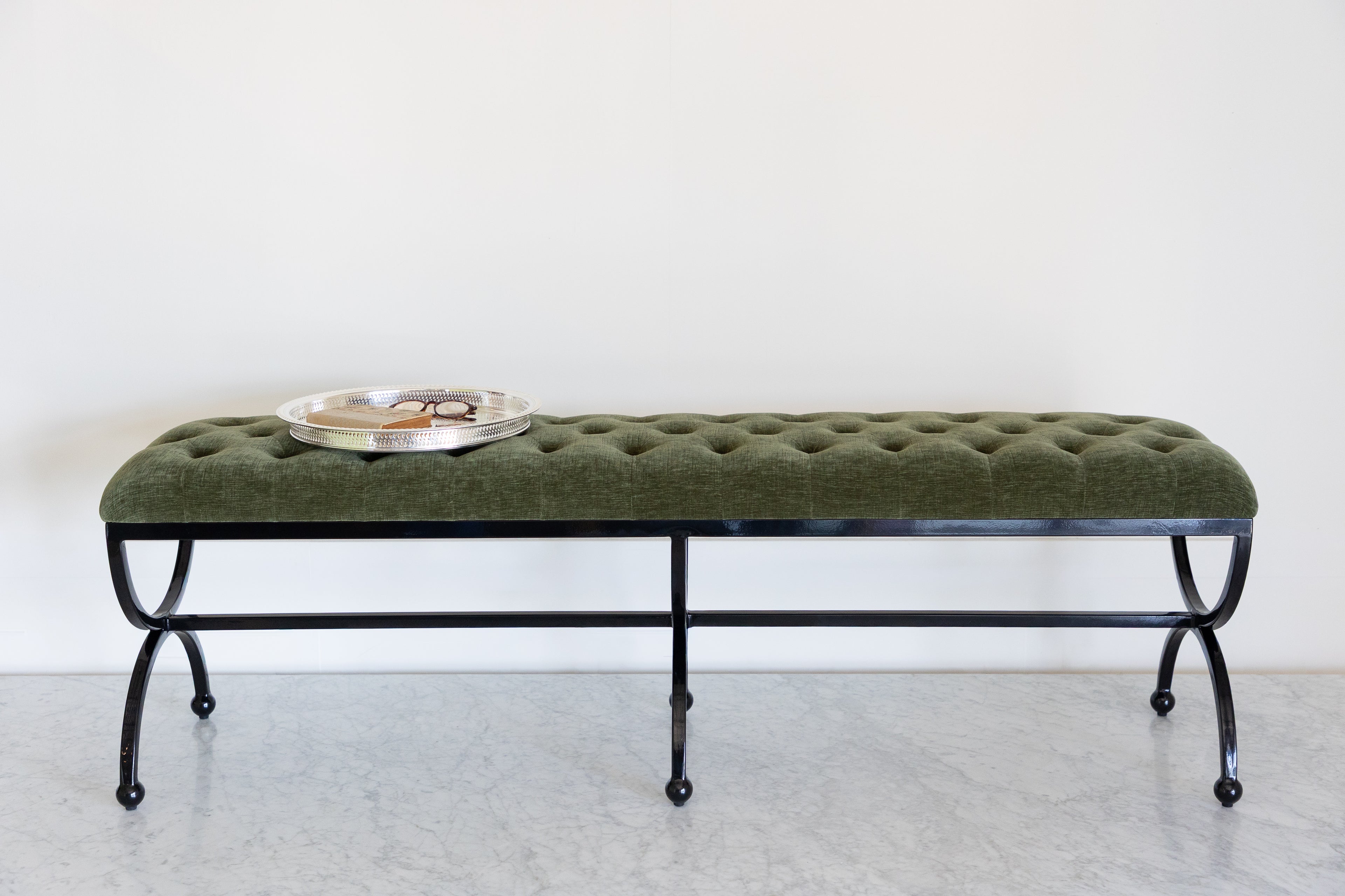 Green upholstered bench with a round metal tray on a white background