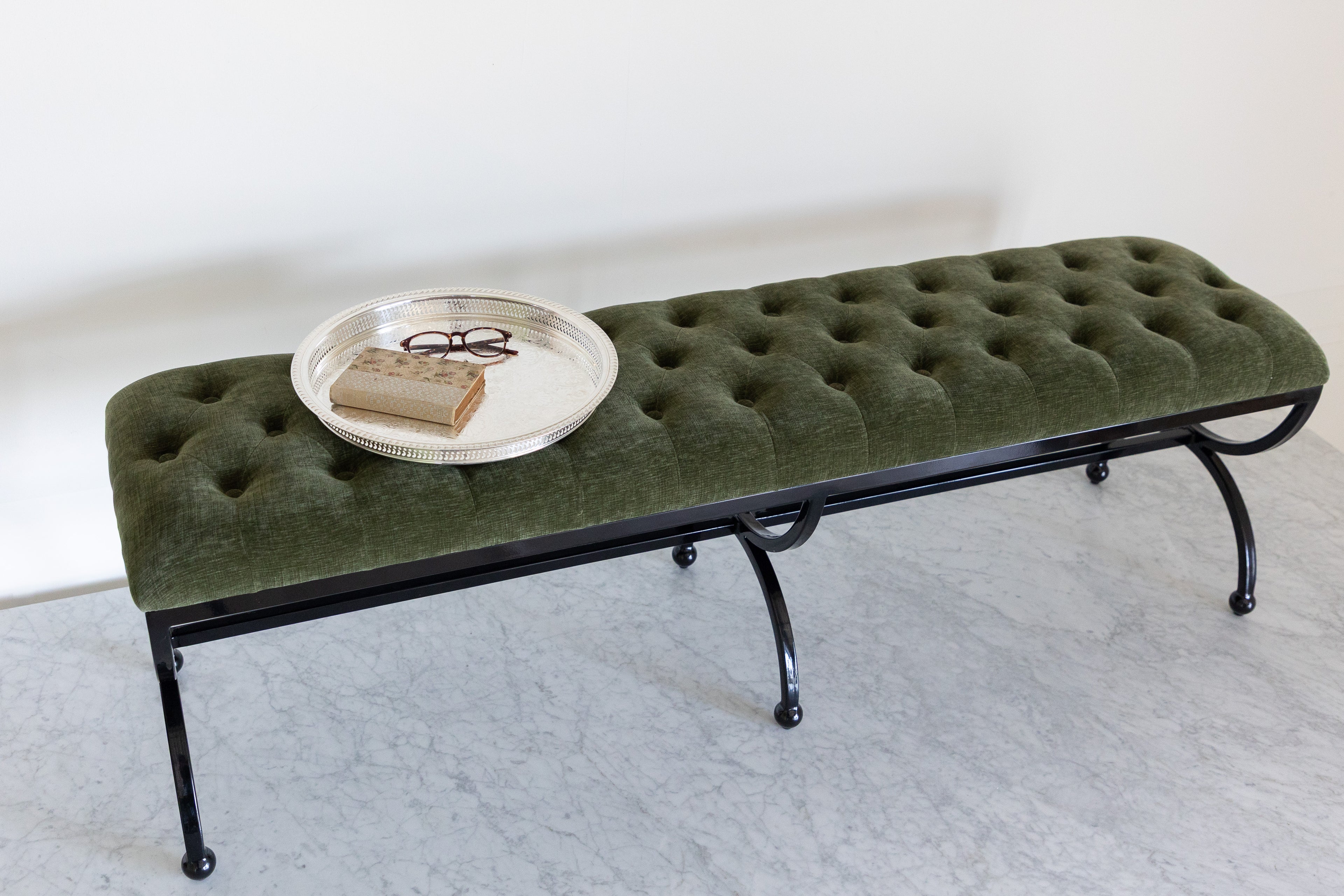 Green upholstered bench with a round metal tray on a white background