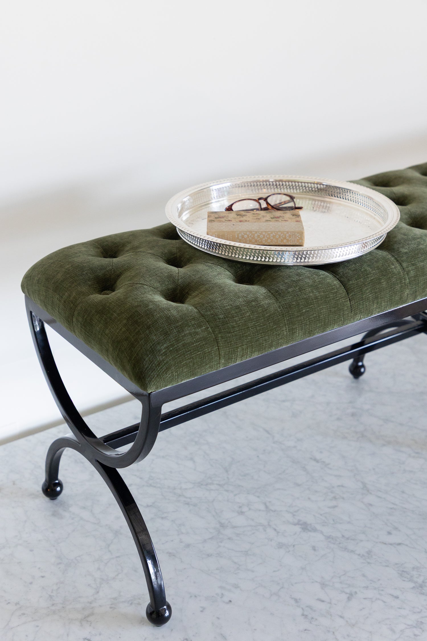 Green upholstered bench with a black metal frame on a light gray floor.