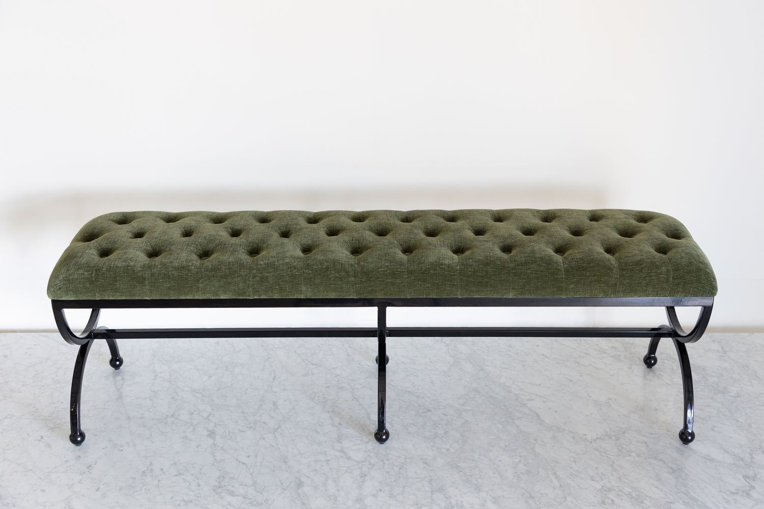 Green tufted bench with black metal legs on a white background