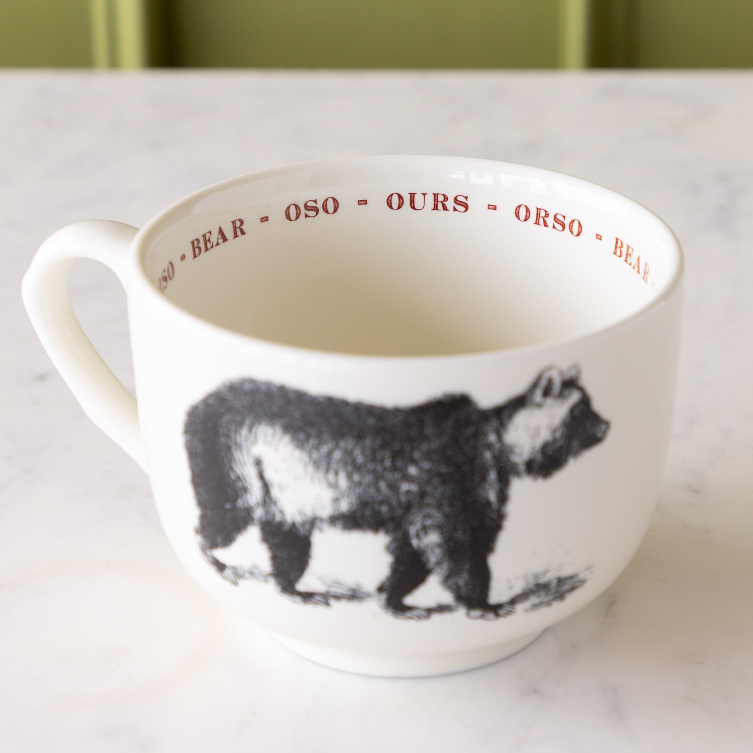 White mug with black bear illustration with &quot;bear&quot; in different languages in red text around the inside rim.