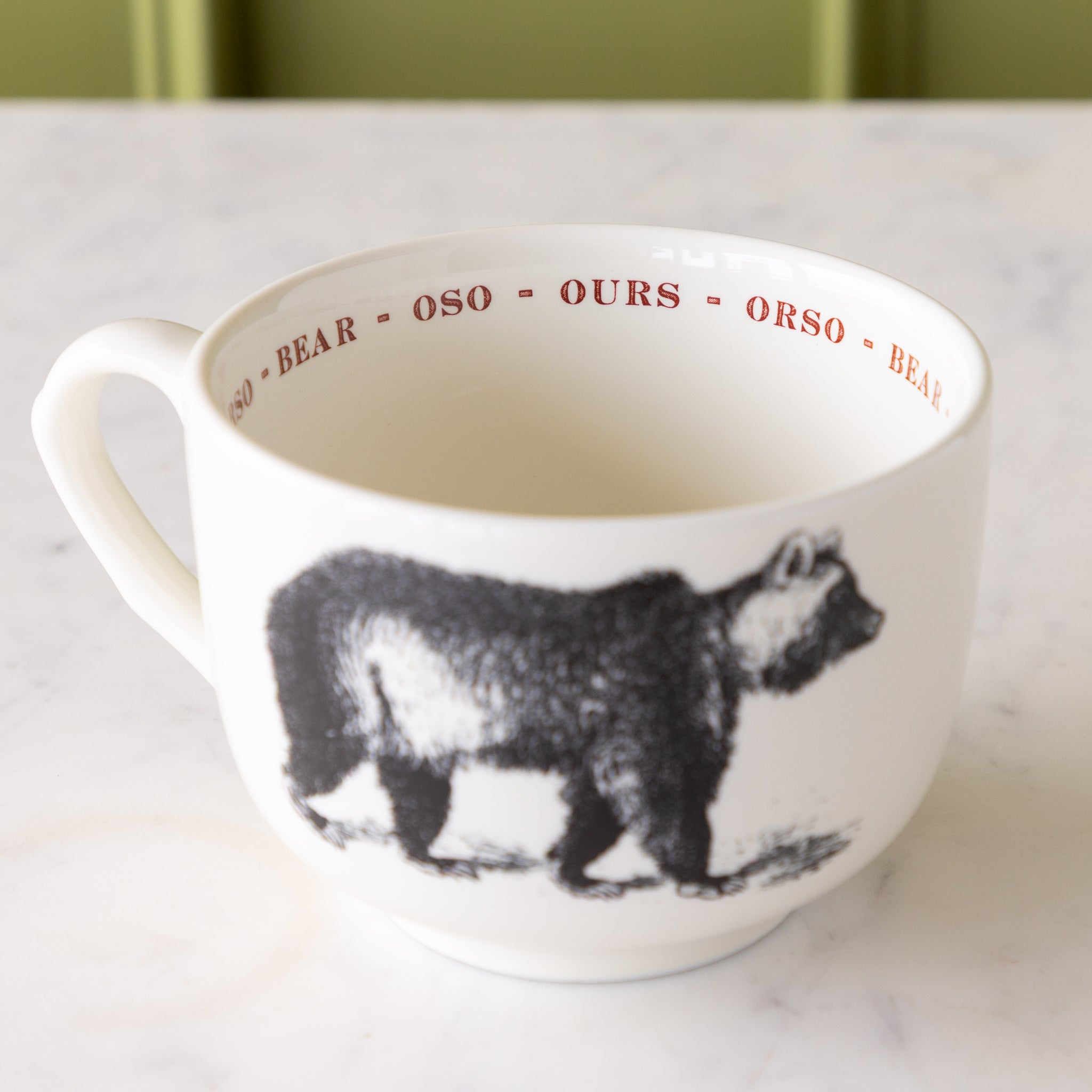 White mug with black bear illustration with &quot;bear&quot; in different languages in red text around the inside rim.