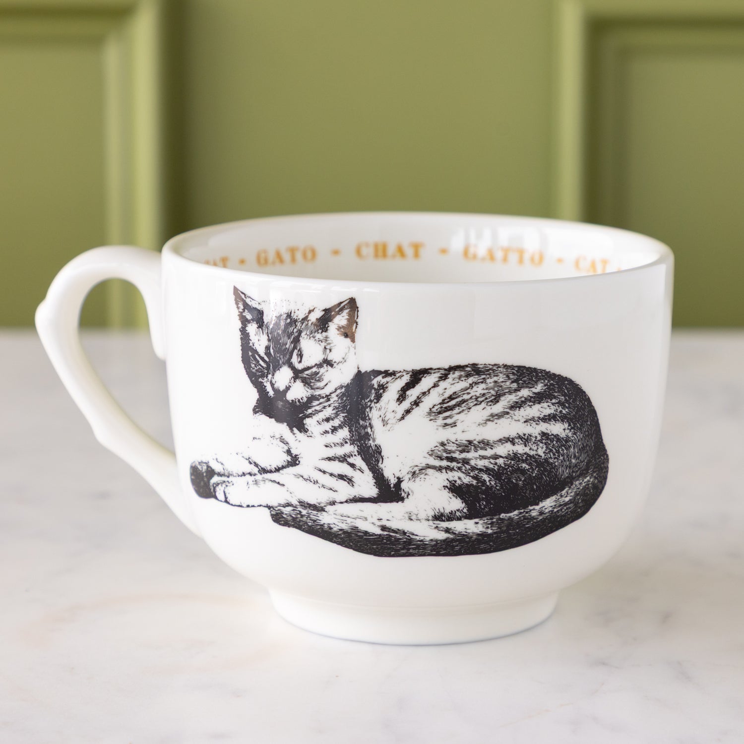White mug with black cat illustration with &quot;cat&quot; in different languages in yellow text around the inside rim.