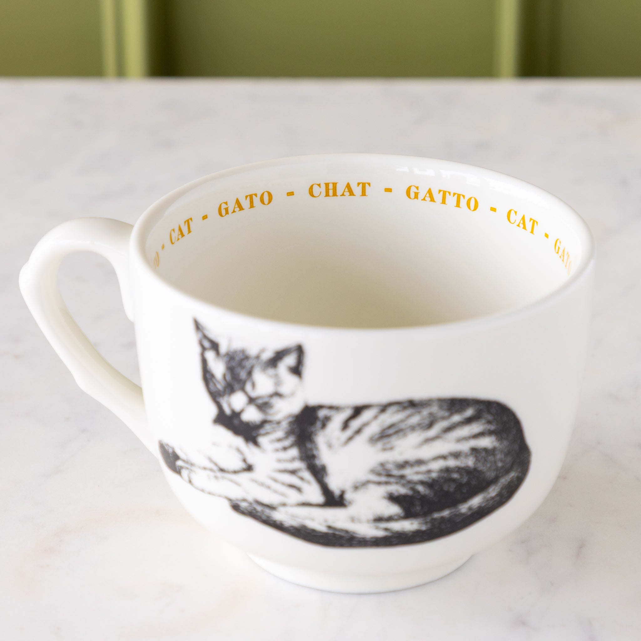 White mug with black cat illustration with &quot;cat&quot; in different languages in yellow text around the inside rim.