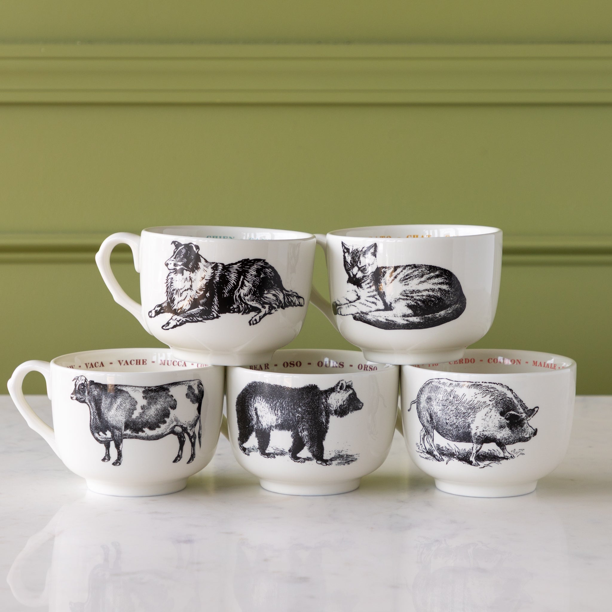 Set of six ceramic mugs with animal illustrations on a light green background.