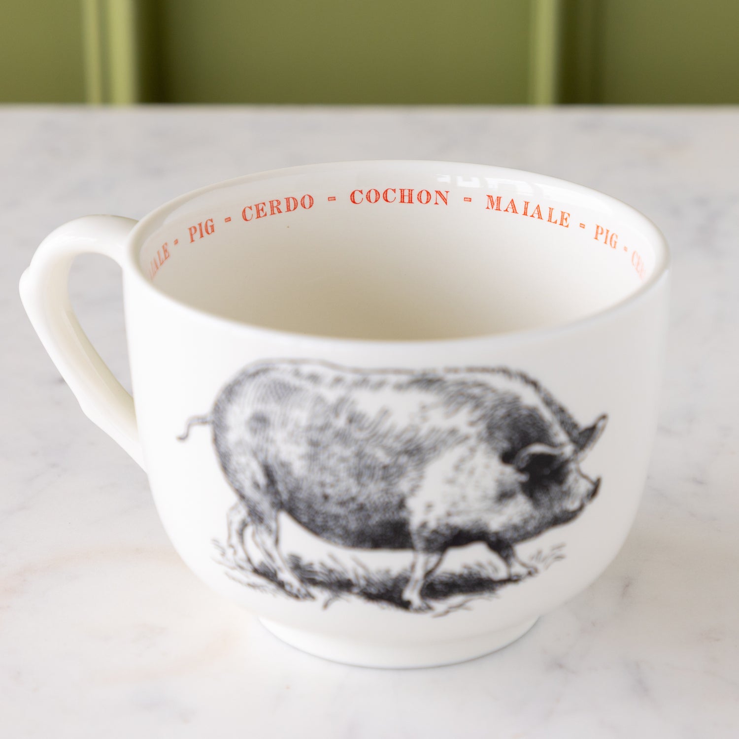 White mug with black pig illustration with &quot;pig&quot; in different languages in red text around the inside rim.