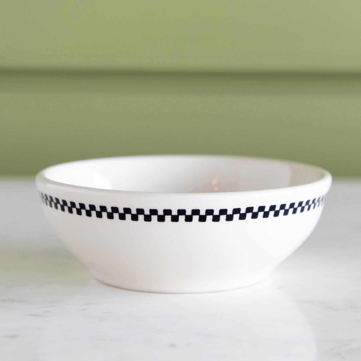 White ceramic bowl with black checkered rim on a light surface with a green background.