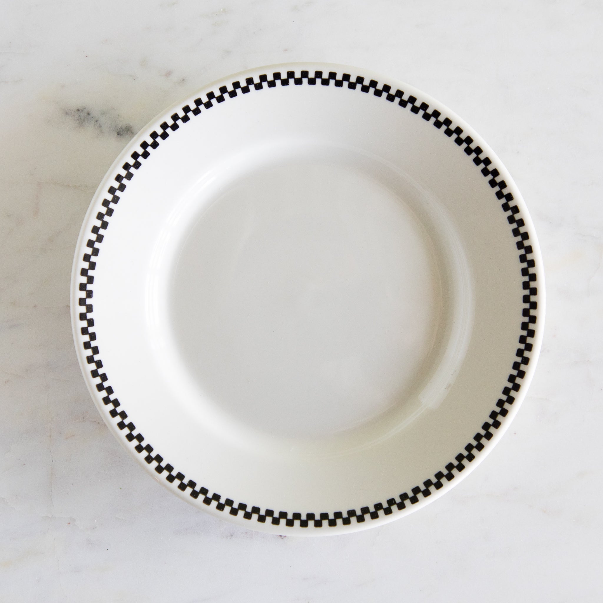 White plate with black checkered rim on a marble surface.