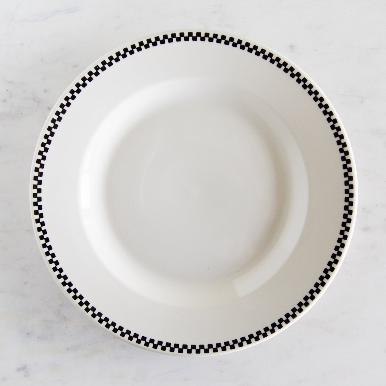 White plate with black checkered rim on a marble surface.
