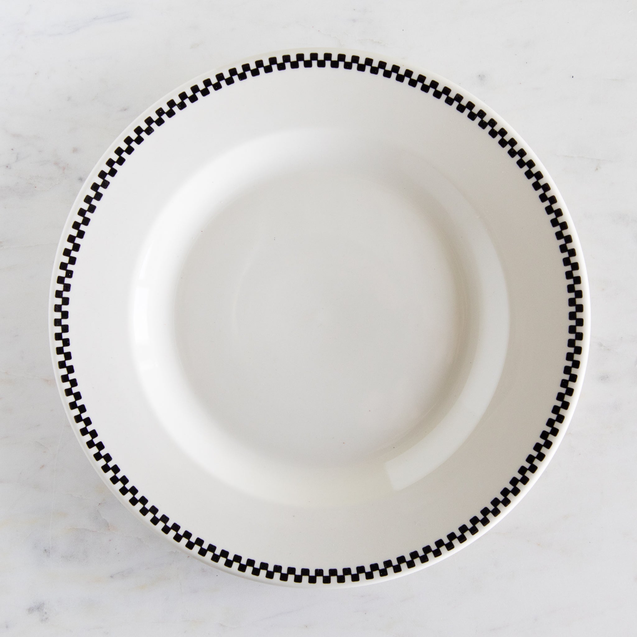 White plate with black checkered rim on a marble surface.