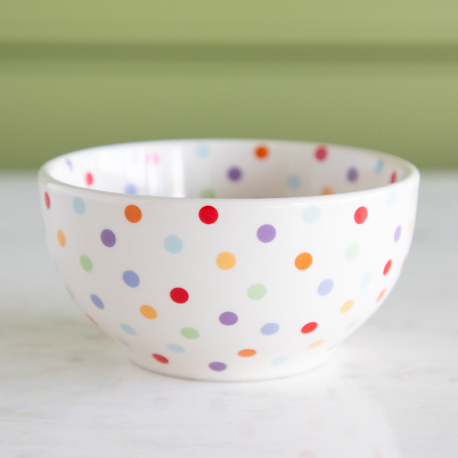 White bowl with colorful polka dot pattern on a white surface with a green background.