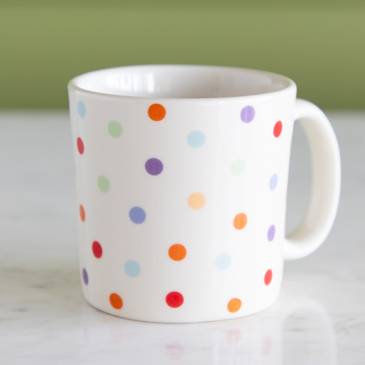 White mug with colorful polka dot pattern on a light background.
