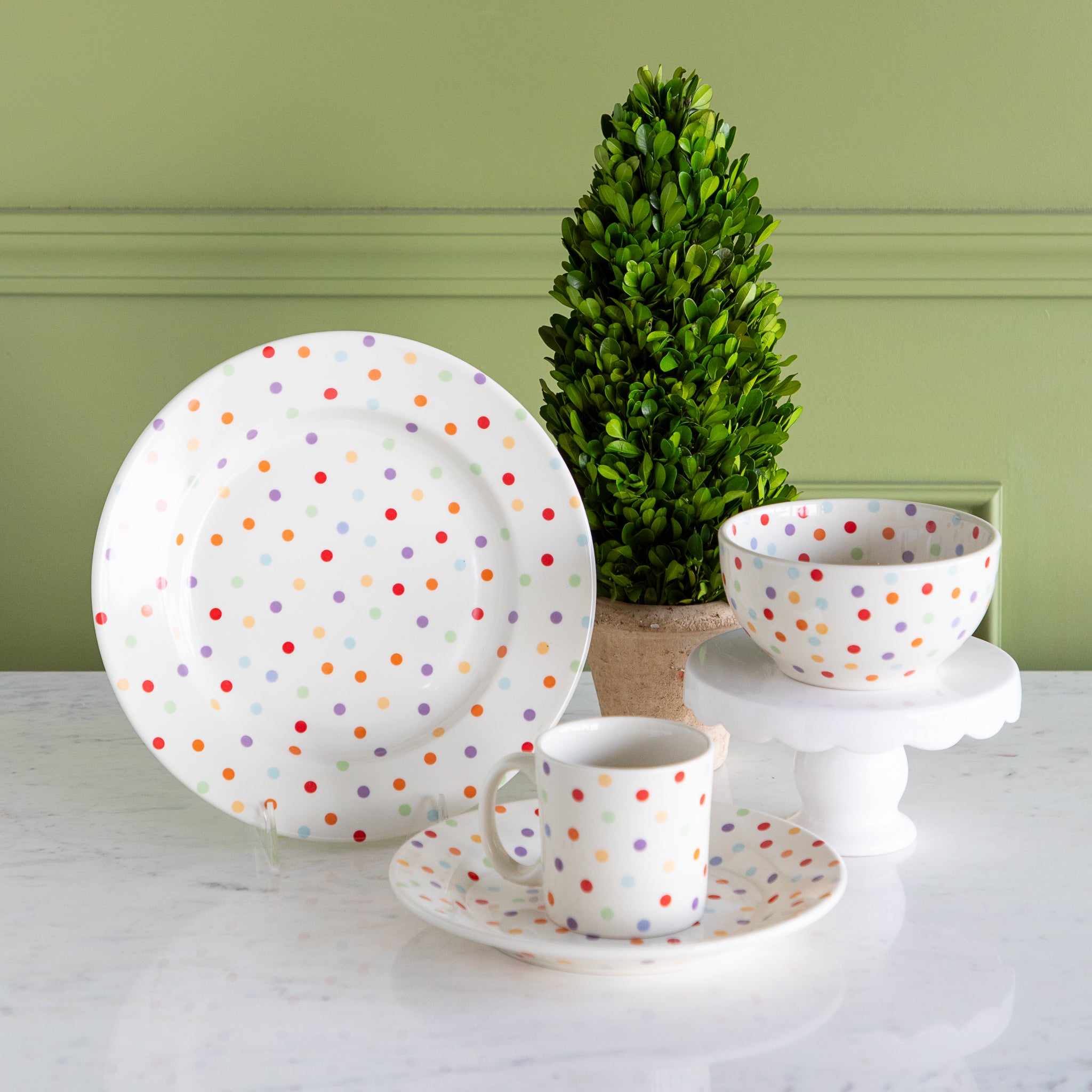 Polka dot ceramic dinnerware set by Fishs Eddy, on a white surface with a green wall background.