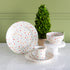 Polka dot ceramic dinnerware set by Fishs Eddy, on a white surface with a green wall background.