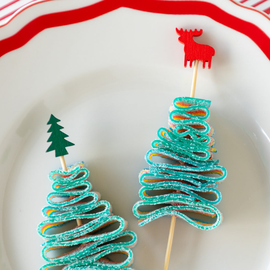 Deer and tree bamboo skewers piercing a candy rainbow rope folded in the shape of a tree, on a decorative plate and Peppermint Stripe Runner underneath.
