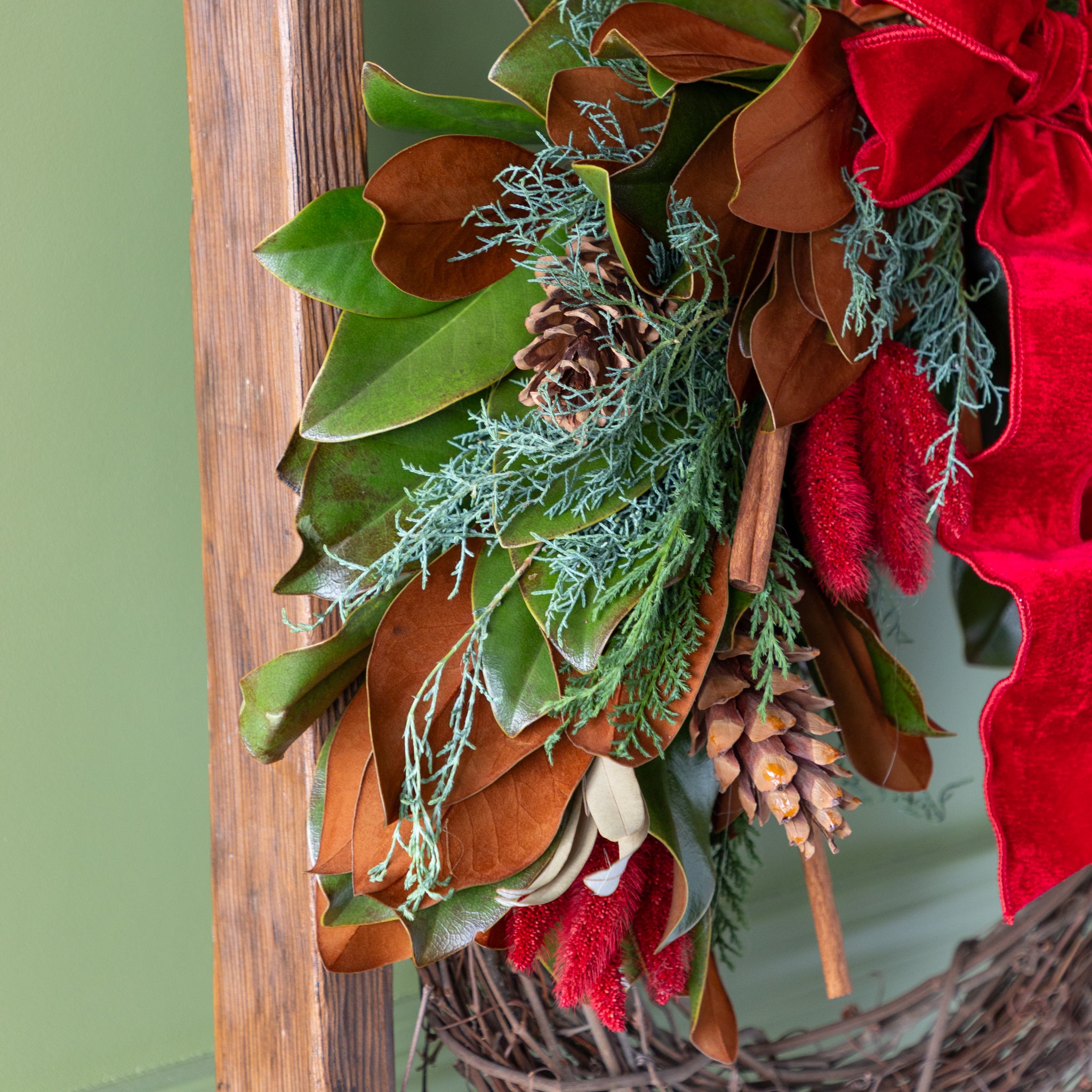 Decorative wreath with green leaves, red berries, and pinecones on a wooden surface.