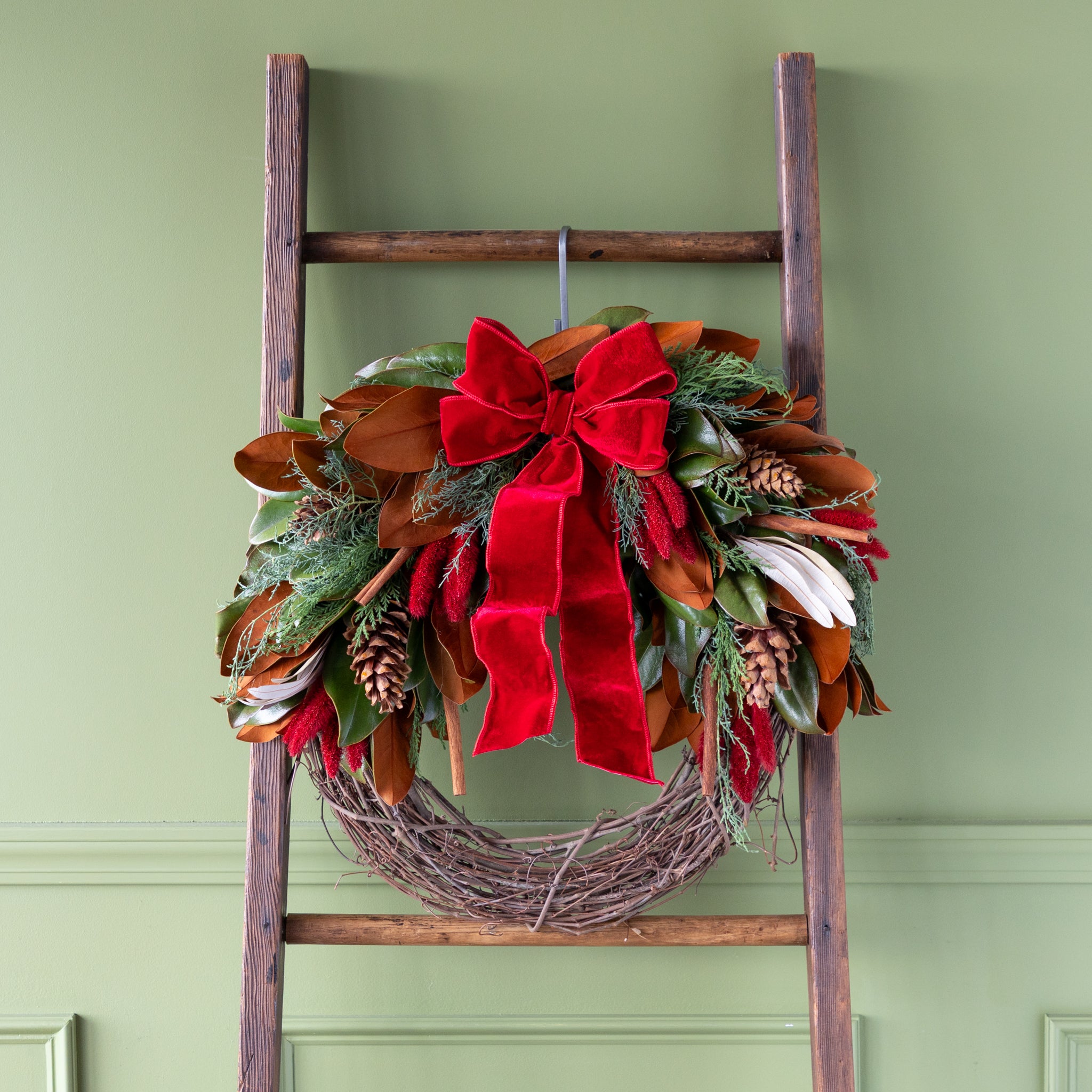 Decorative wreath with a red bow on a wooden ladder against a green wall