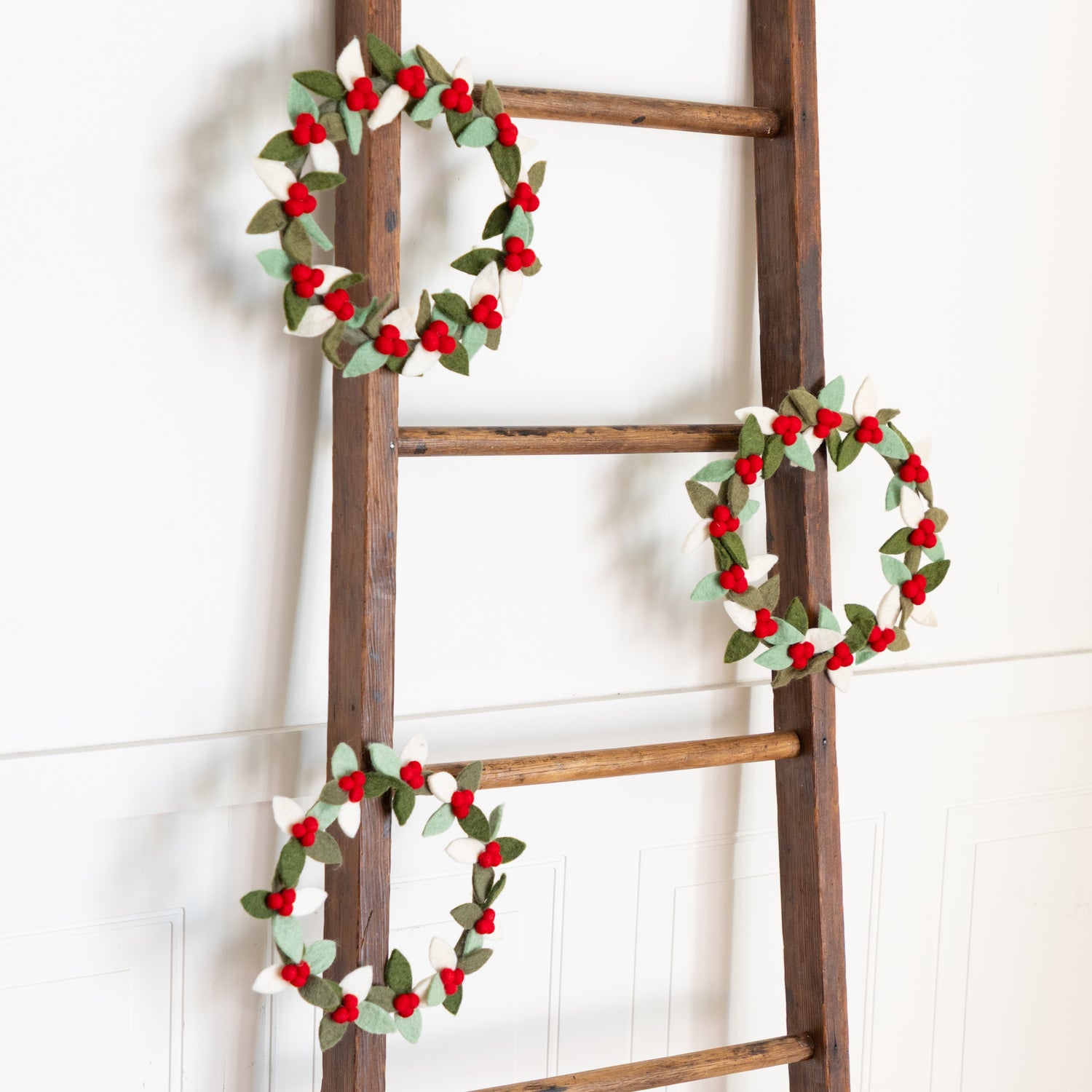 Wooden ladder with three Felt Berry Wreaths on a white background.