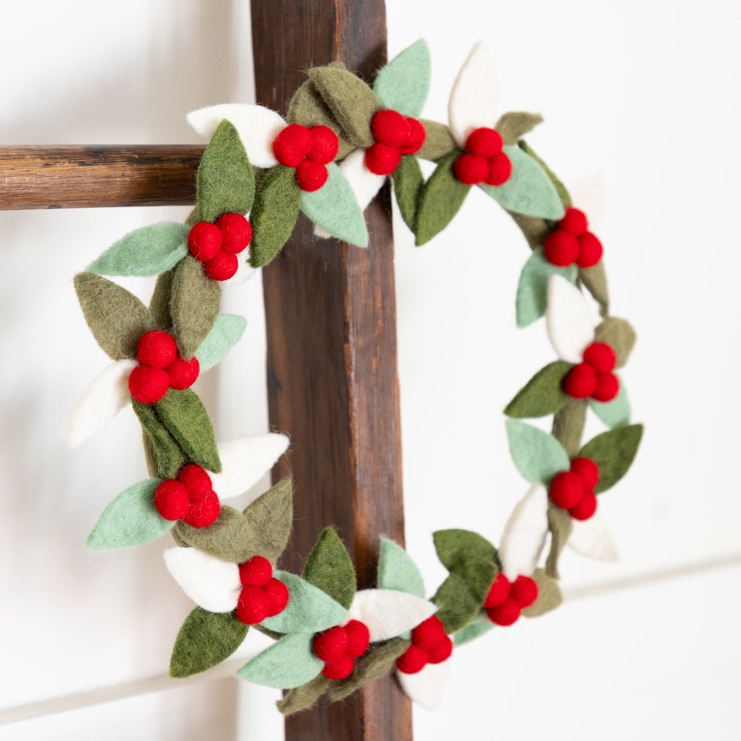 Felt wreath with red berries and green leaves on a wooden ladder.