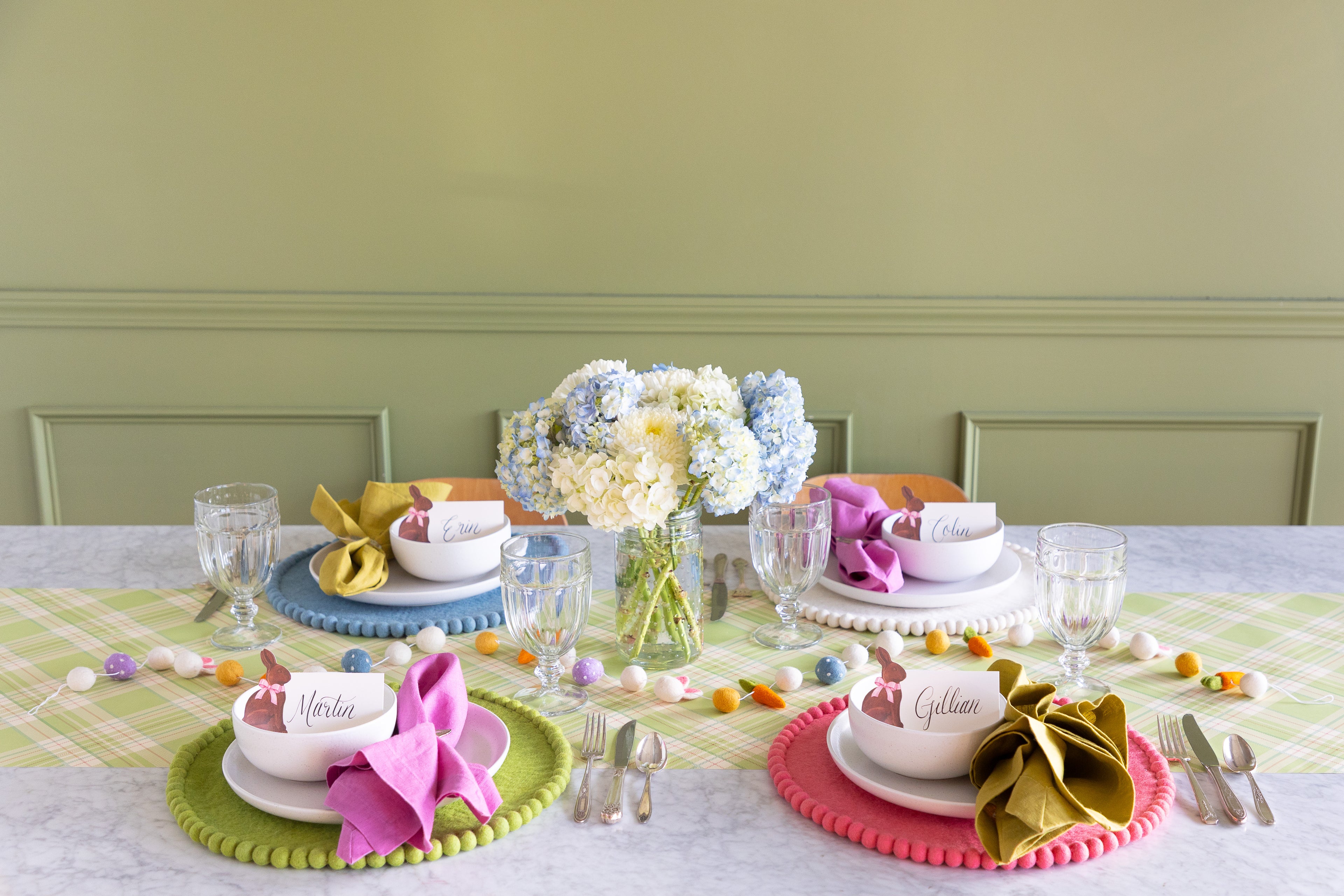 Easter-themed table setting with a floral centerpiece, Easter Felt Garland, Pink, Cornflower Blue, Spring Green and White Pom Pom Felt Placemats, and Hershey&
