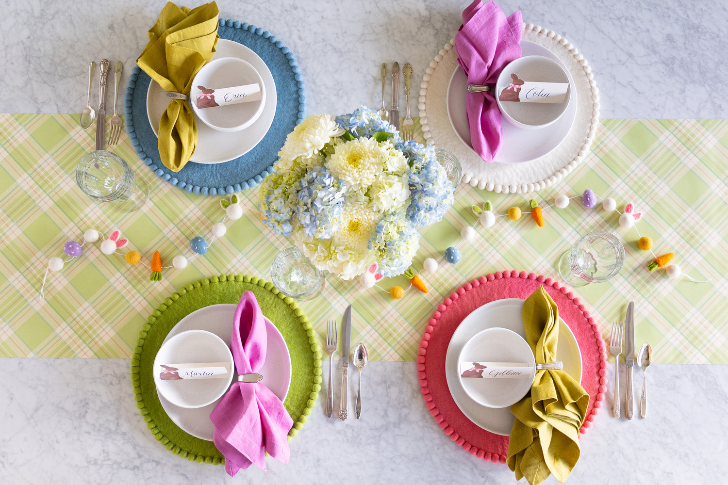 Easter-themed table setting with a floral centerpiece, Easter Felt Garland, Pink, Cornflower Blue, Spring Green and White Pom Pom Felt Placemats, and Hershey&