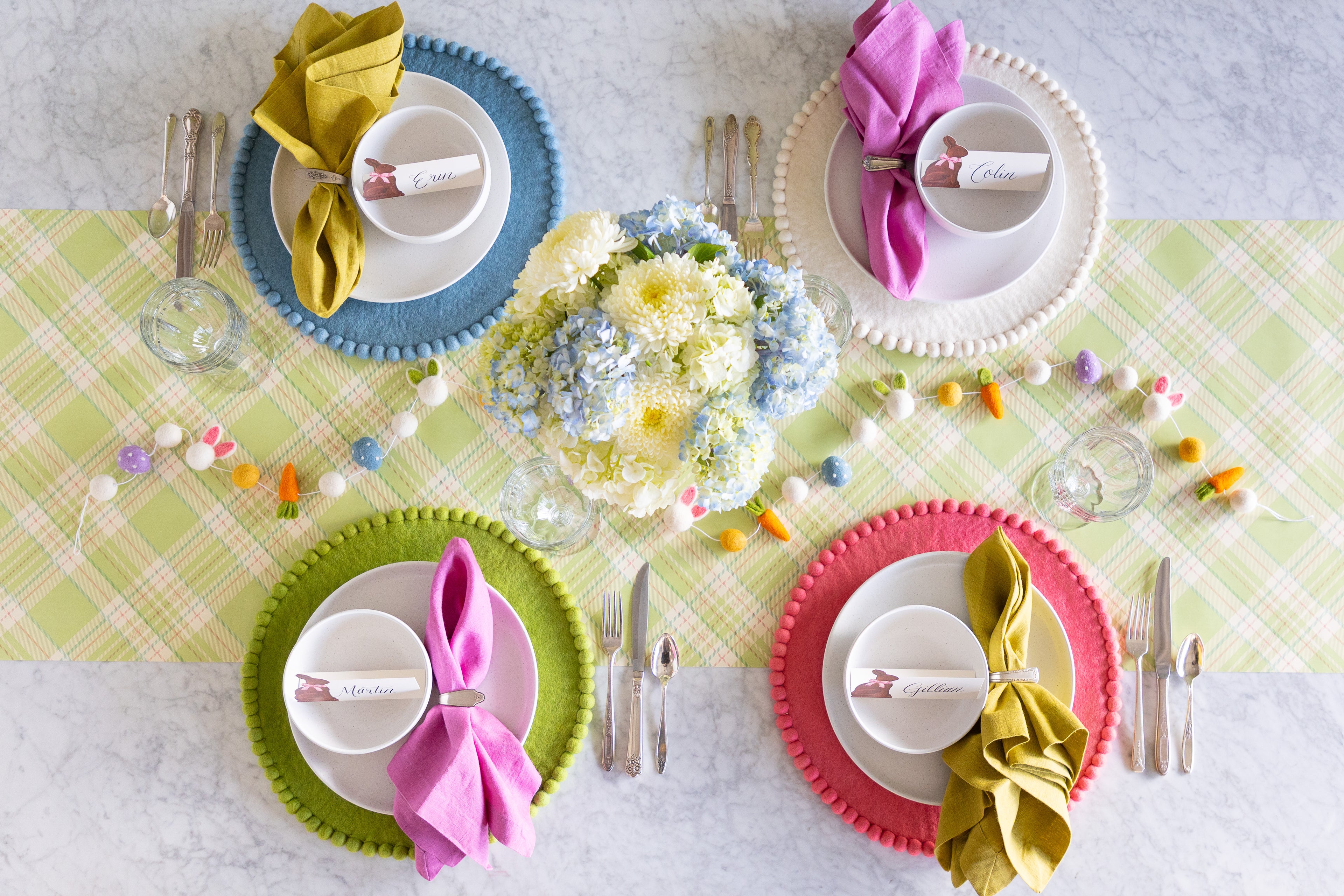 Easter-themed table setting with a floral centerpiece, Easter Felt Garland, Pink, Cornflower Blue, Spring Green and White Pom Pom Felt Placemats, and Hershey&