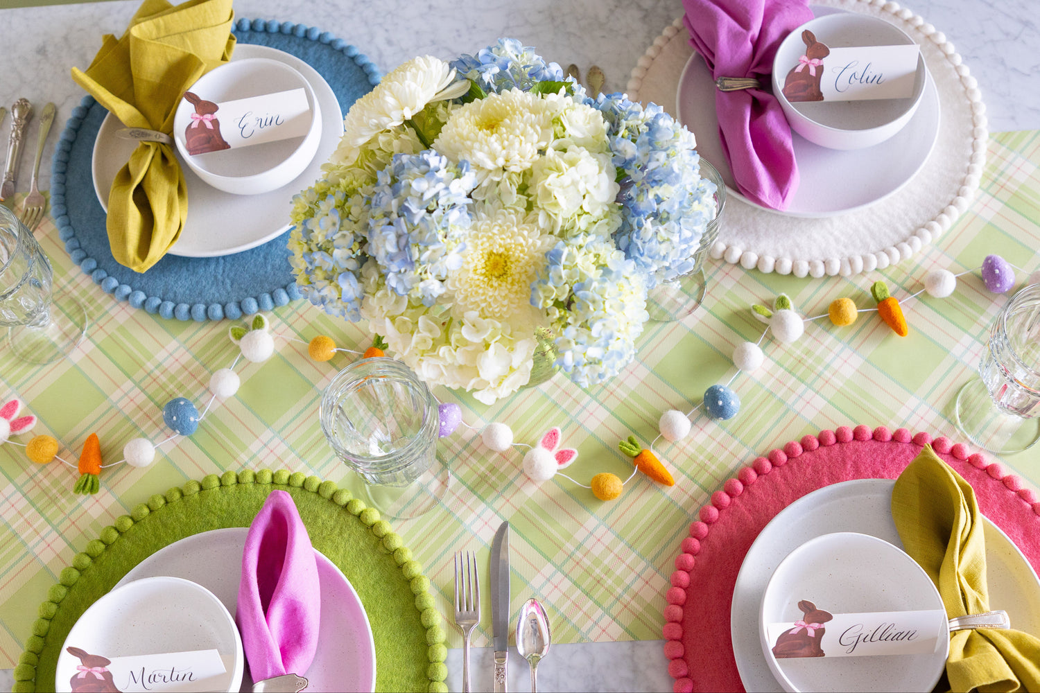 Easter-themed table setting featuring the Easter Felt Garland, flowers, Spring Green, Ivory, Cornflower Blue and Pink Felt Pom Pom Placemats and Hershey&