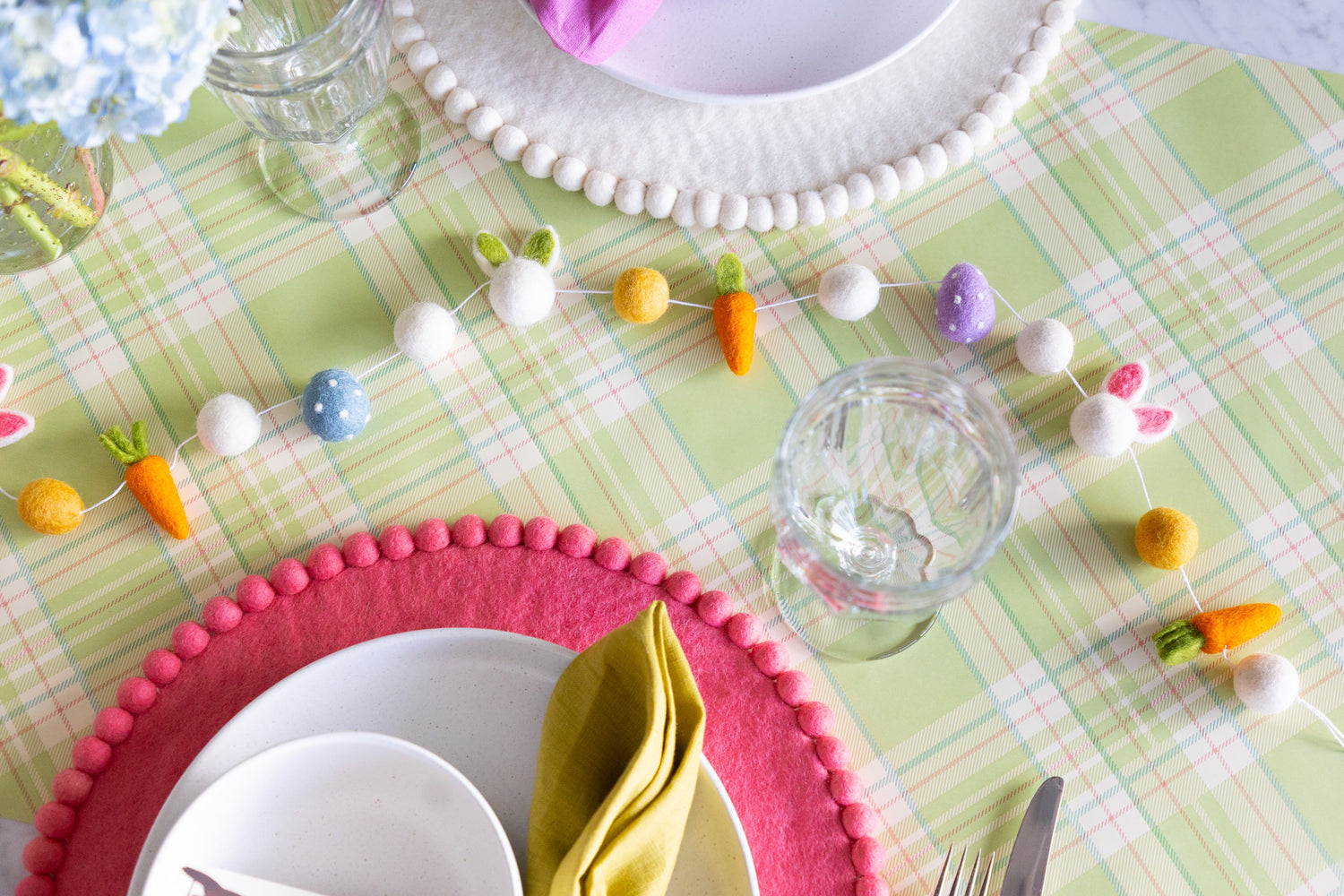 Easter-themed table setting with Pink and White Pom Pom Felt Placemats and Easter Felt Garland on the Green Plaid Runner.