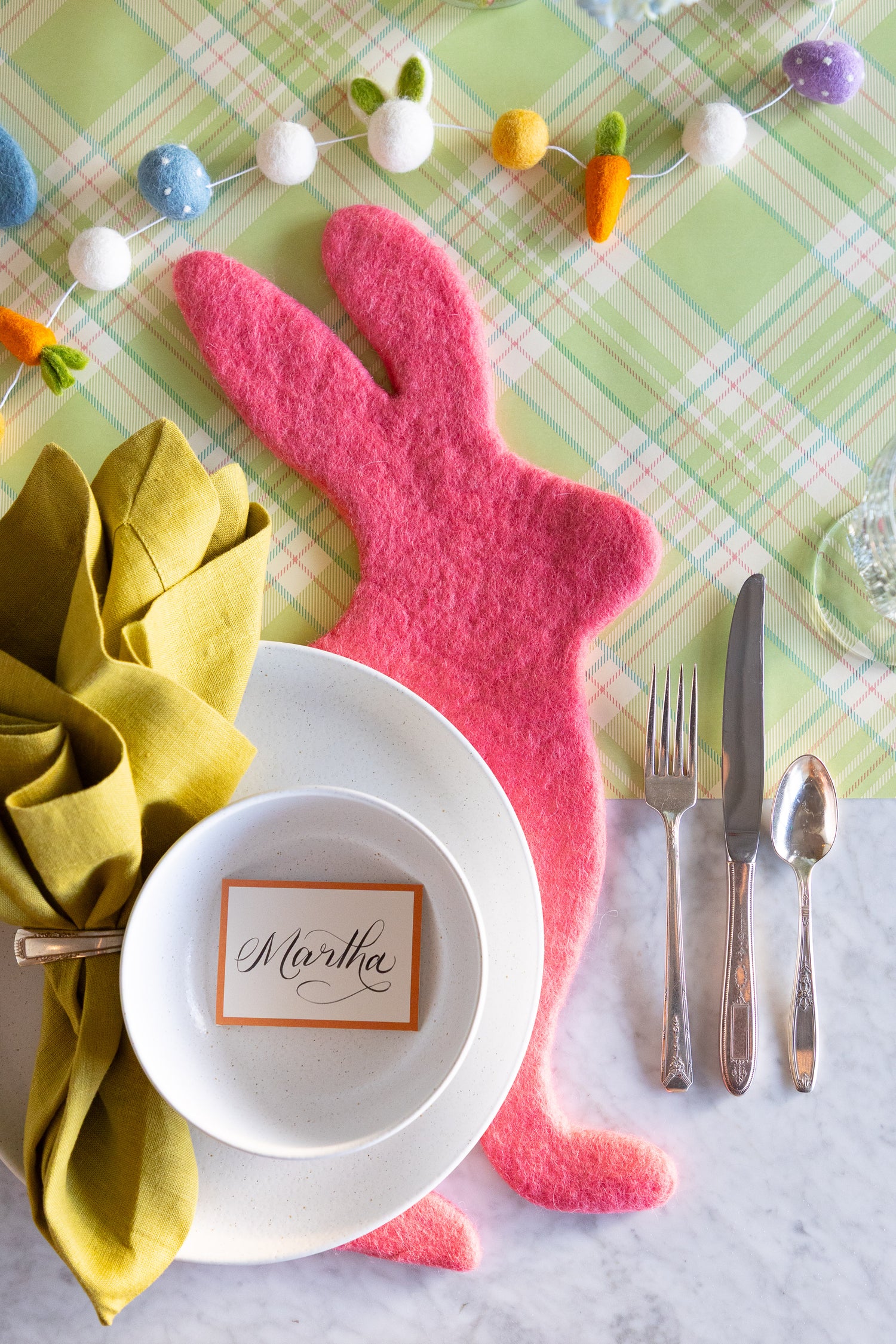 Easter table setting with the Pink Bunny Felt Placemat, dinnerware, Orange Frame Place Card and Easter Felt Garland on the Green Plaid Runner.