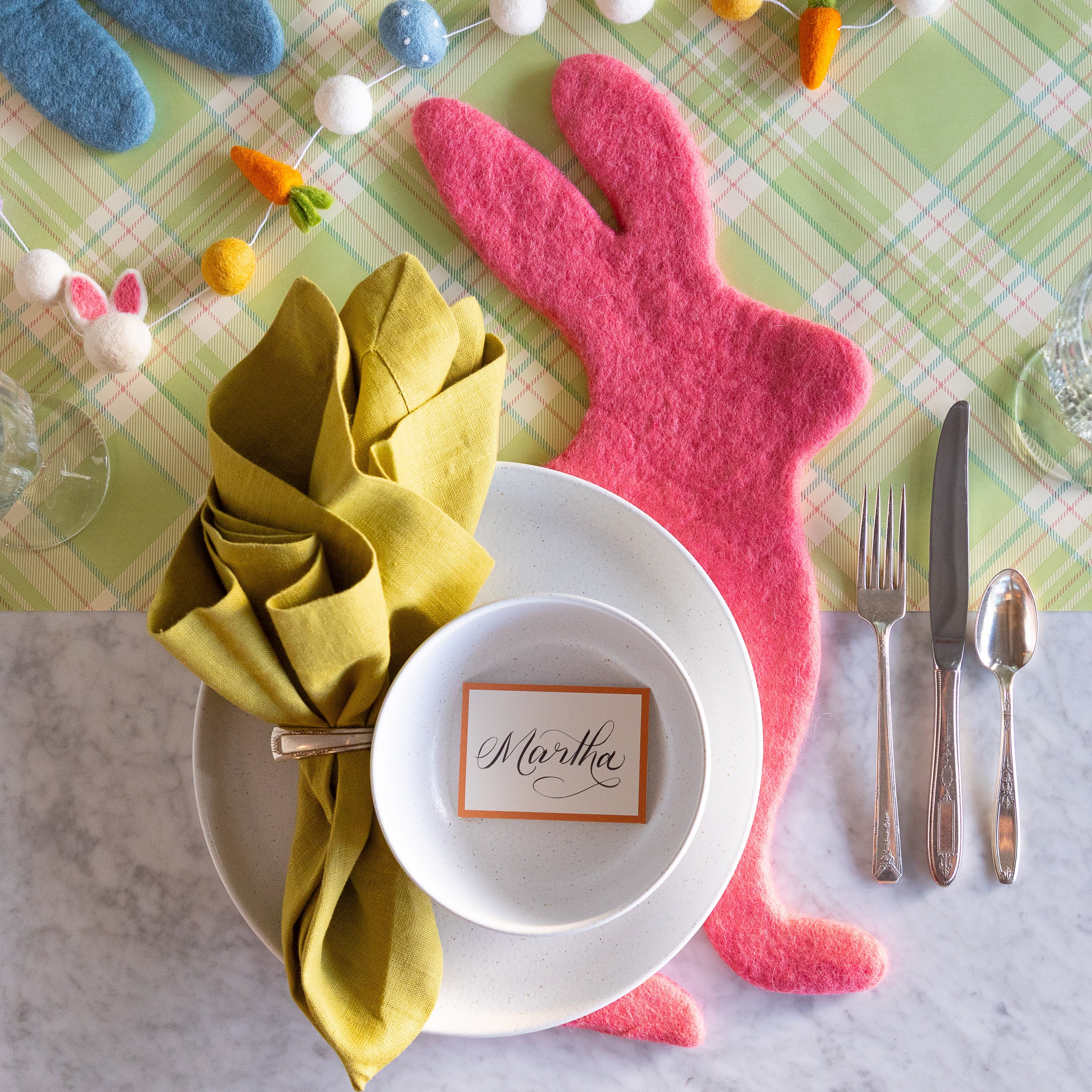 Easter-themed table setting with Pink Bunny Felt Placemat, colorful napkin, and place card on the Green Plaid Runner.