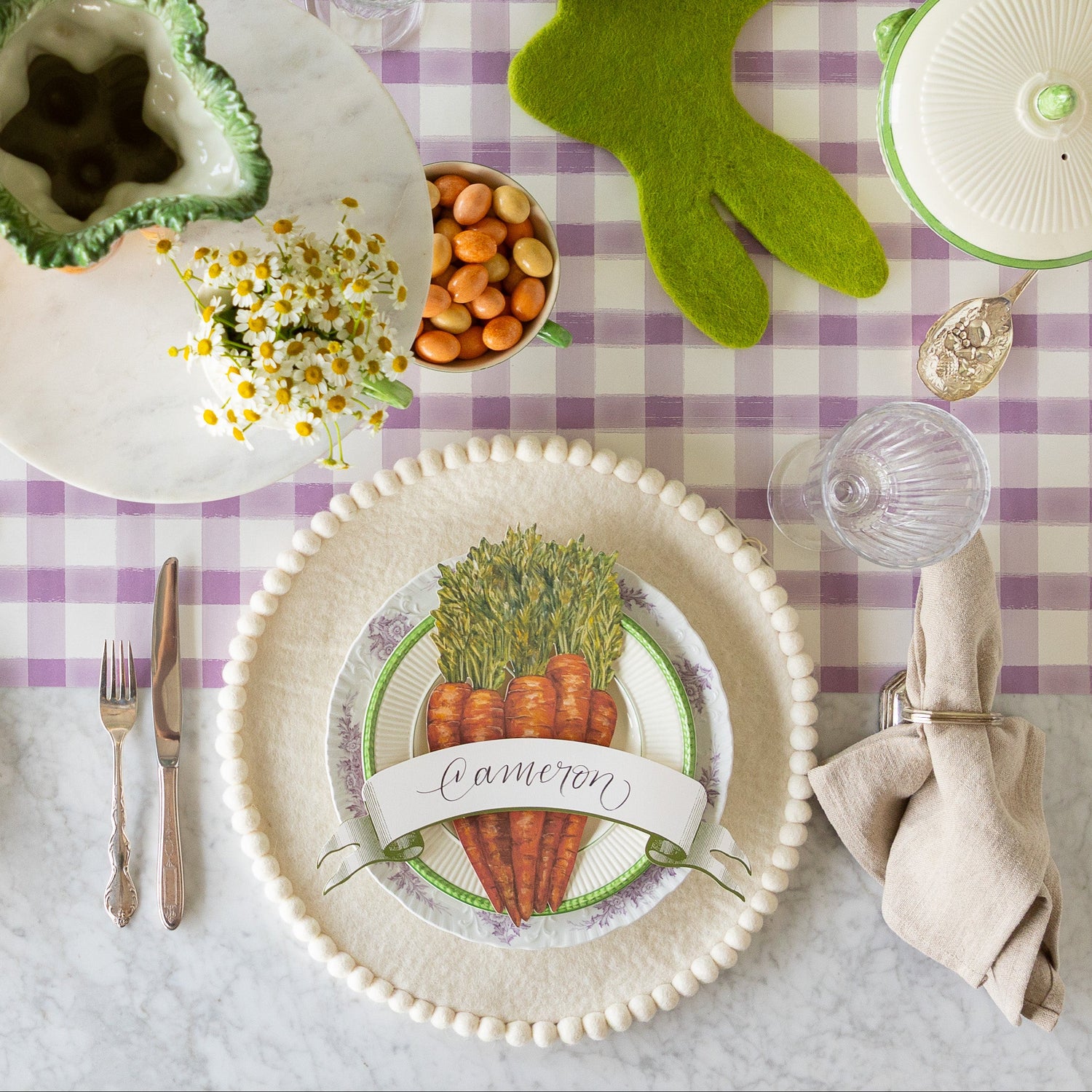 Easter table setting with the Ivory Felt Pom Pom Placemat, decorative plates, Carrots &amp; Moss Classic Banner Table Accents on the Lilac Painted Check Runner.